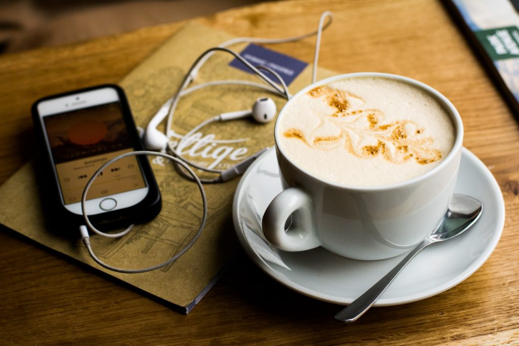 A coffee, a notebook, and a phone playing a playlist.
