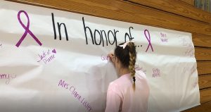 A girl signs a poster in honor of a breast cancer survivor close to her.